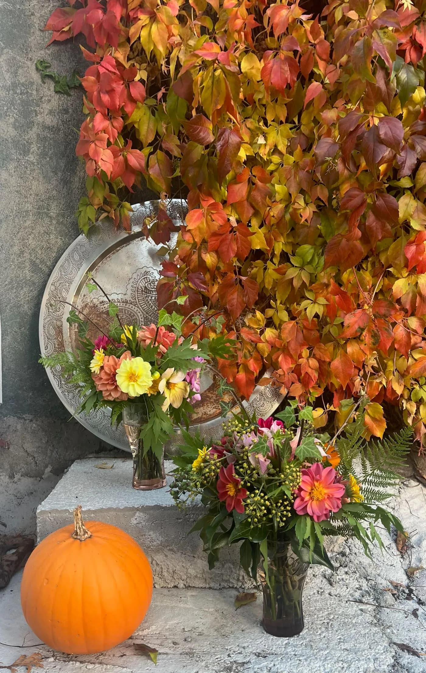 Höstblommor och pumpa i ett naturligt arrangemang vid en stenmur — omsorg och säsongens växlingar